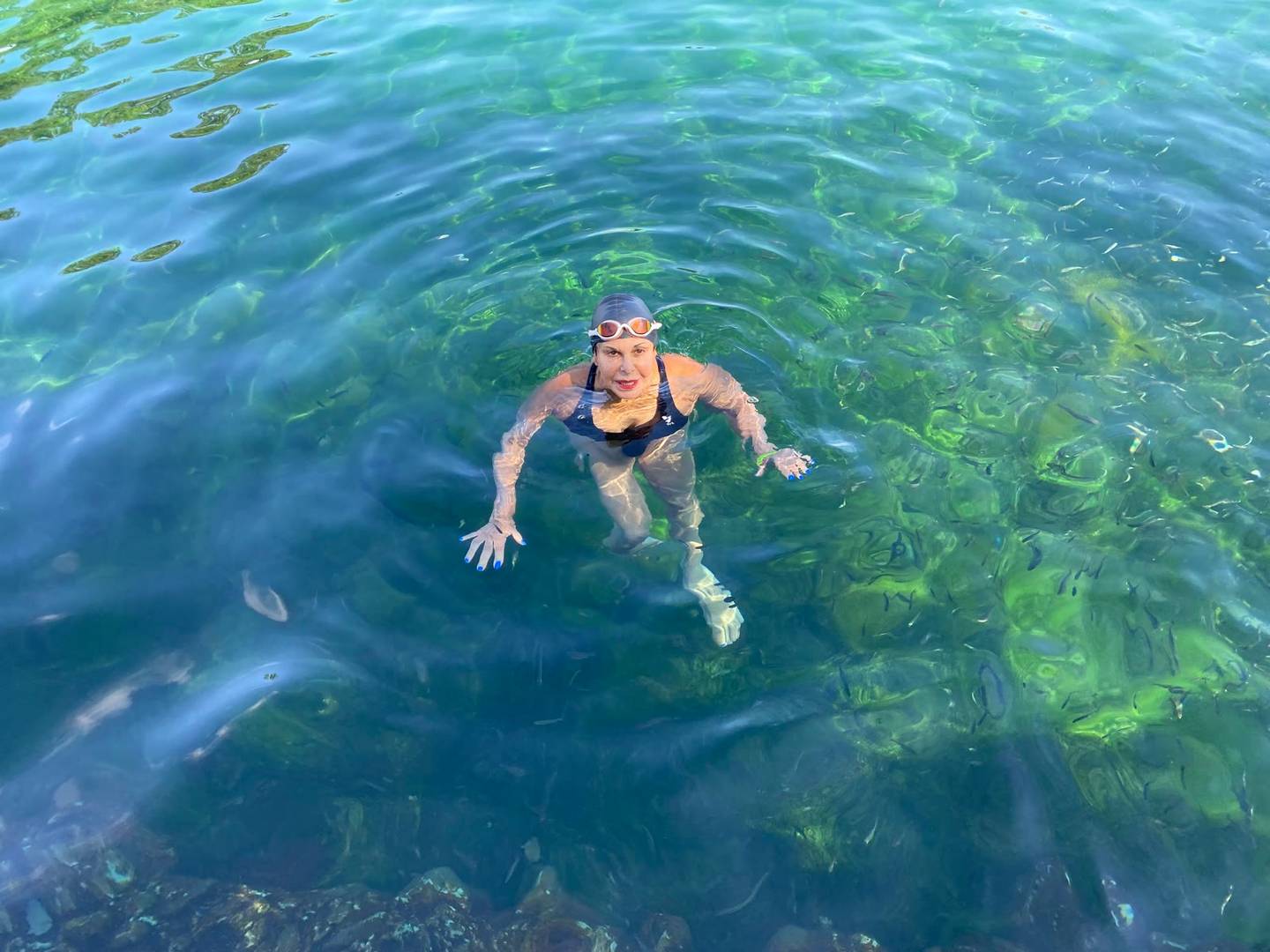 A swimmer in cap and goggles smiling up from the crystal-clear turquoise water of Balmorhea pool