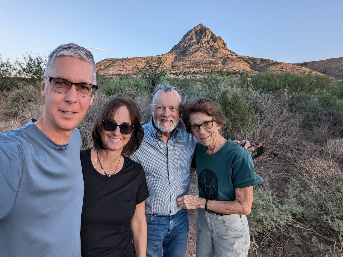 Four campers in a selfie in front of a sunlit rocky peak at dusk