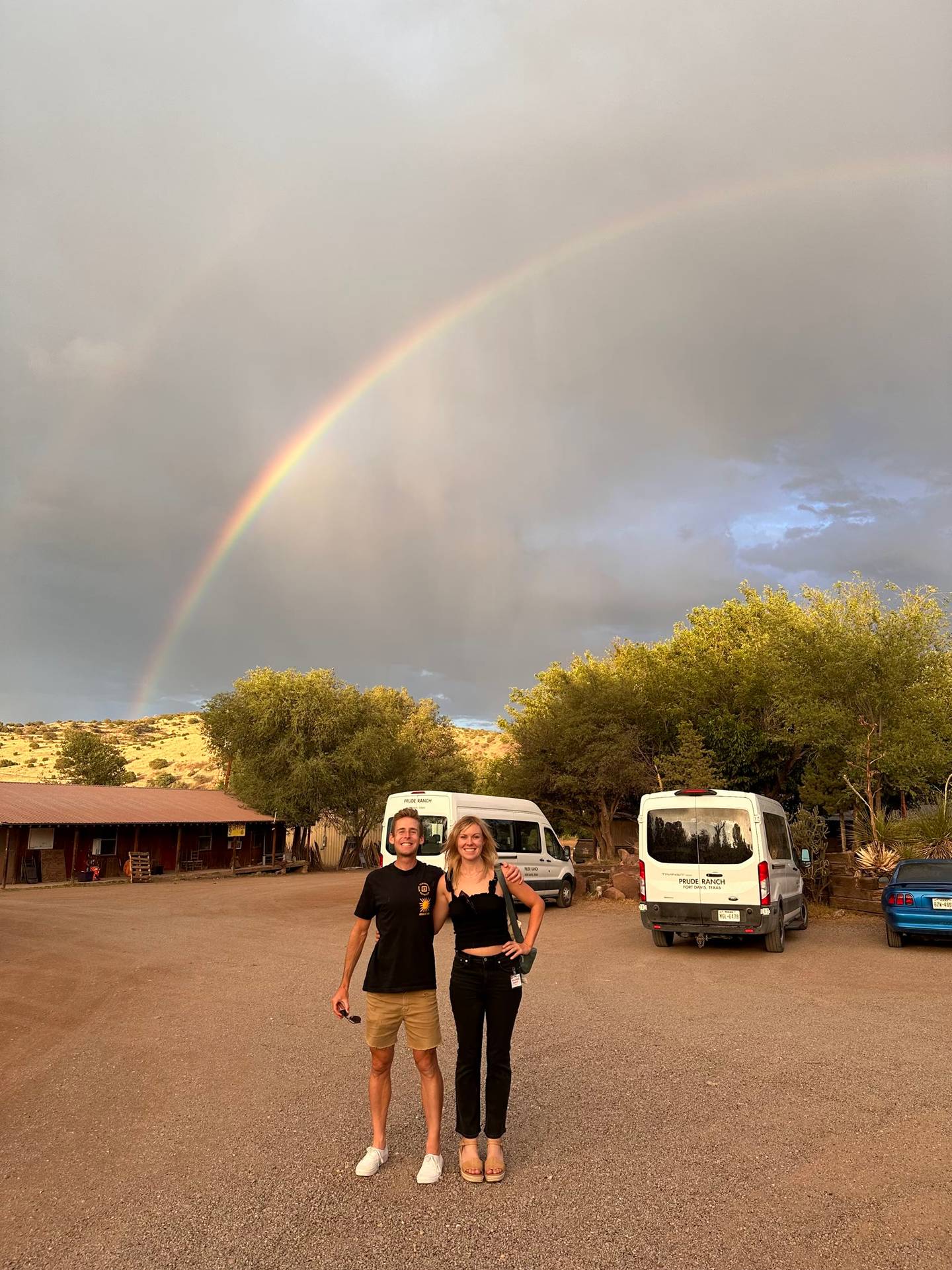 A rainbow arcing over the red-roofed ranch buildings and white camp vans at Prude Ranch