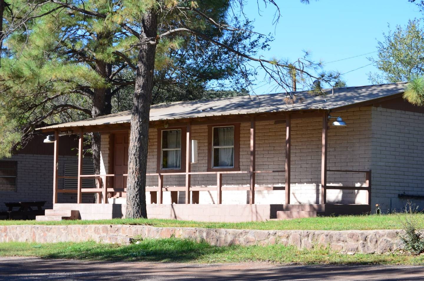 A long single-storey bunkhouse with a covered porch, shaded by tall pines